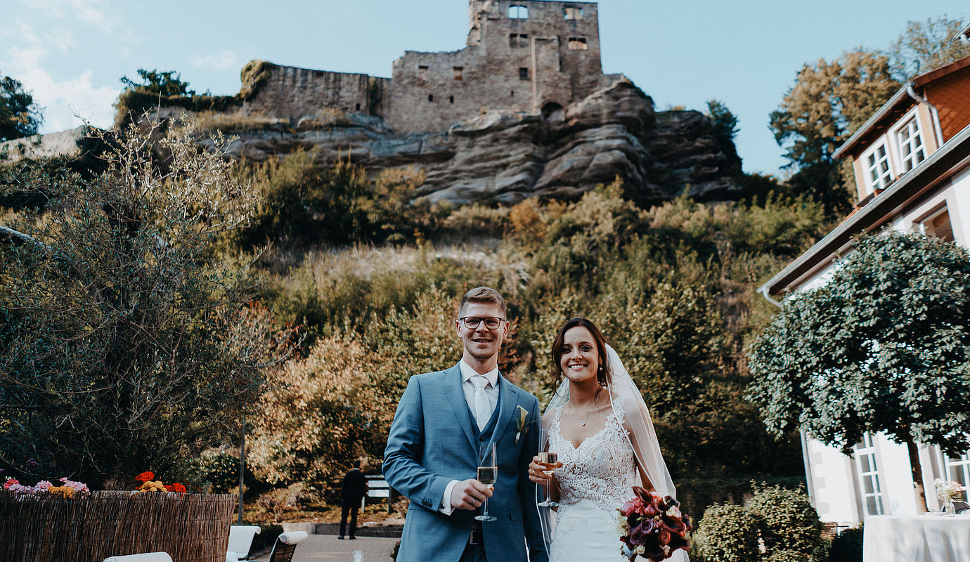 Braut und Bräutigam lächeln in die Kamera mit einem Glas Sekt in der Hand während ihrer Hochzeit in Niedersachsen.