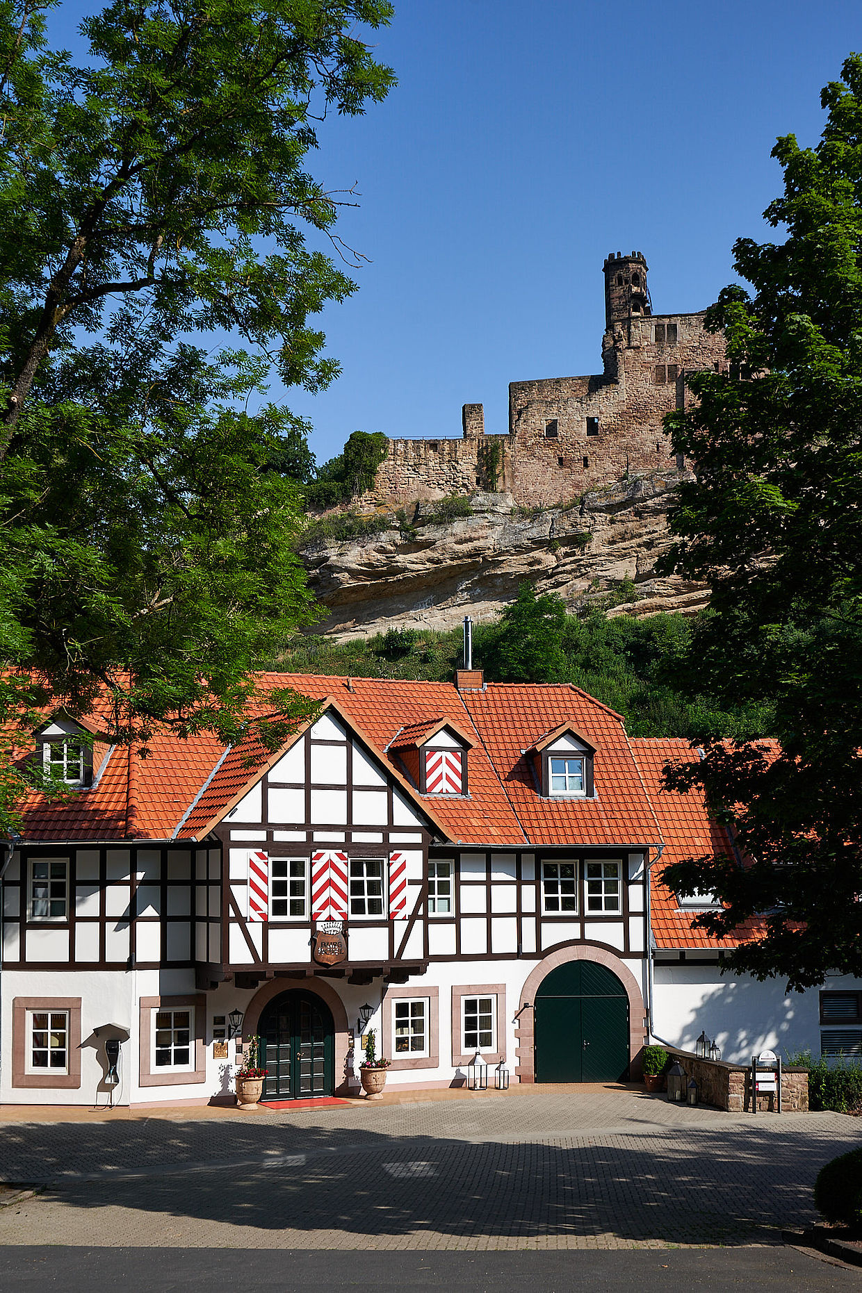 Das Fachwerkhaus des BurgHotels Hardenberg mit rotem Dach und Blick auf eine mittelalterliche Burgruine.