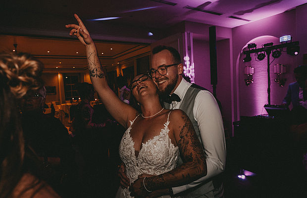 Fröhliches Brautpaar tanzt bei Hochzeitsparty mit Lichteffekten.