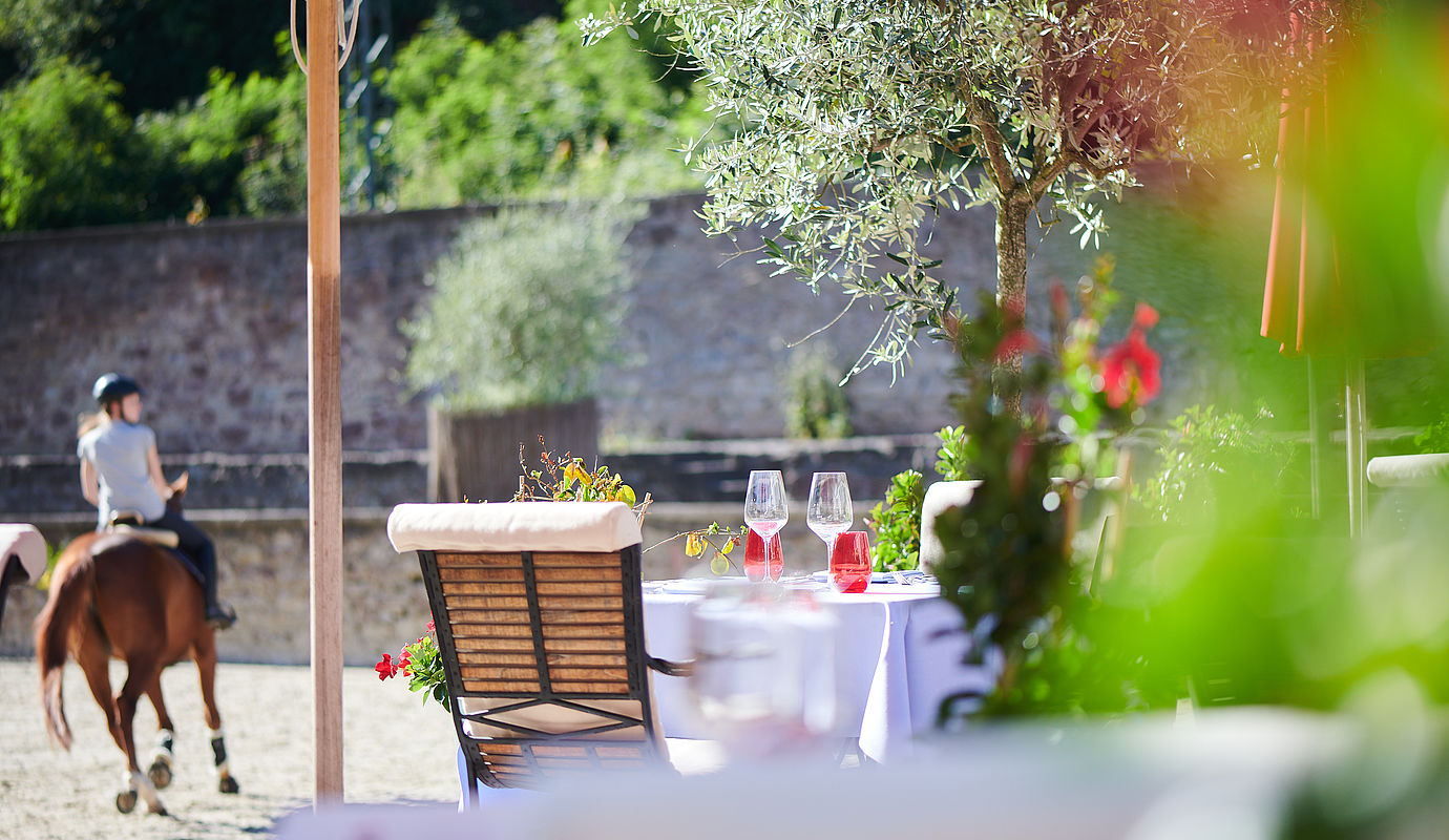 Außenterrasse des Restaurants und ein Mädchen auf einem Pferd im Hintergrund.