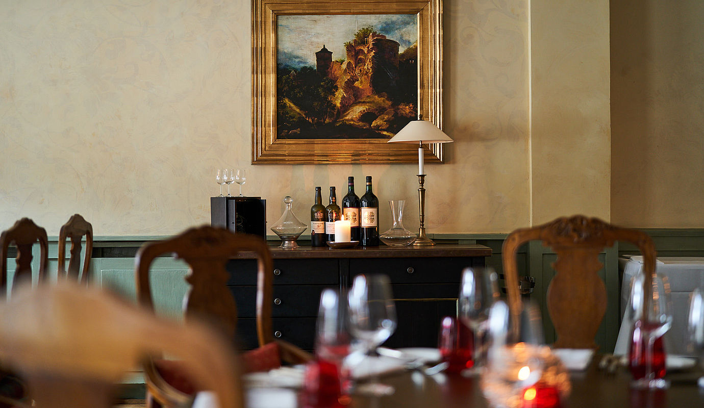 Tische und eine Kommode mit Weinflaschen unter einem Bild der Hardenberg BurgRuine im Novalis-Restaurant