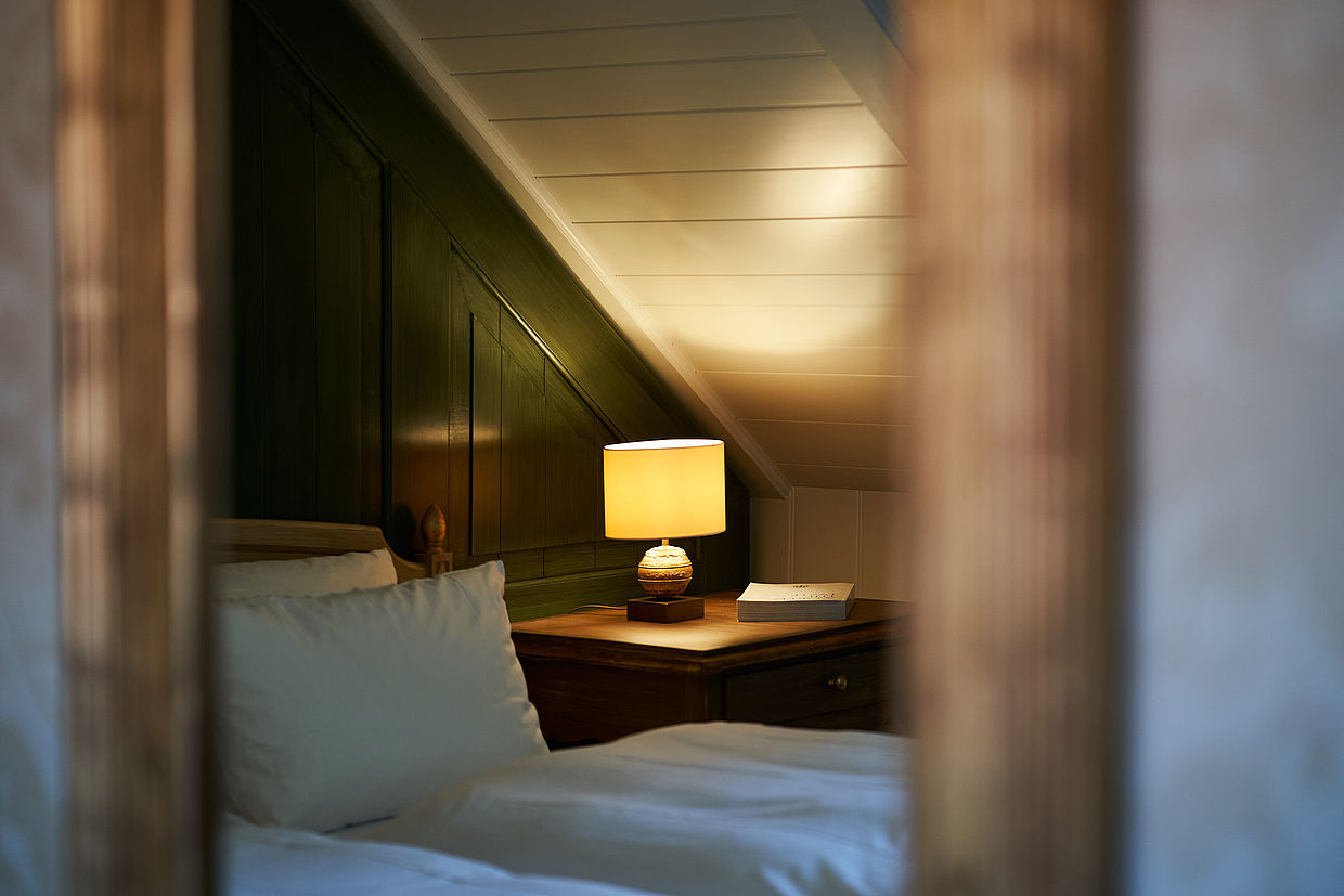 Nahaufnahme aus einem Fenster auf ein Bett und eine Nachtlampe daneben im Hardenberg BurgHotel
